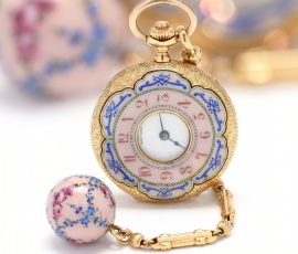 Vintage decorative gold pocket watch with floral detailing and porcelain accent bead